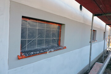 An exterior wall which is covered with prime and partially rendered, a glass block window and a...