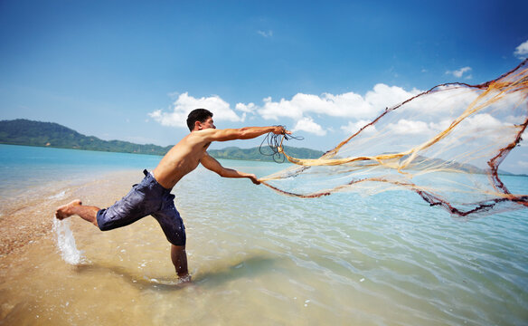 Casting his nets. Shot of a traditional thai fisherman standing in the water casting a net into the ocean.