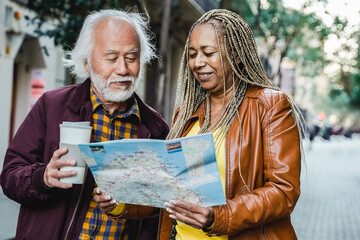 Multiracial senior couple looking for directions on map outdoor - Elderly travelers and healthy lifestyle - Focus on African woman face