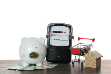 Electricity meter, house model, piggy bank and shopping cart with money on wooden table against...