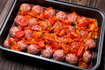 Raw meatballs with vegetables on a baking sheet are ready to bake in the oven. selective focus