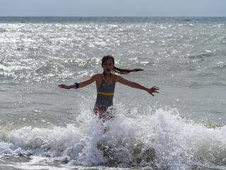 A girl in a striped swimsuit with long hair runs into the sea wave