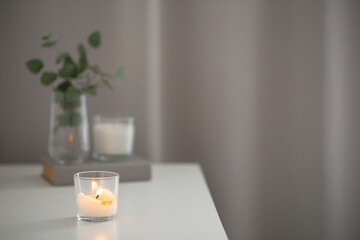 Home interior decor with burning candle, book and glass vase with eucalyptus branch.