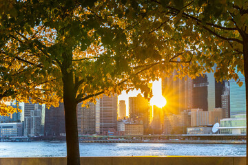 The sun sets among Midtown Manhattan skyscraper beyond the East River on November 2021 in New City. View from Franklin D. Roosevelt Four Freedoms Park at Roosevelt Island.