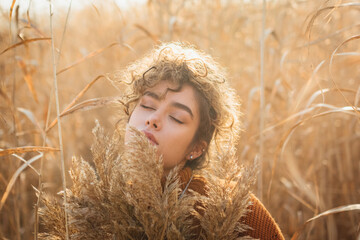 Portrait of beautiful young woman with curly hair posing in the reed with sunset backlight
