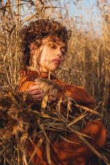 Portrait of beautiful young woman while posing outdoor and holds bouquet of reeds