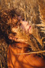Portrait of beautiful young woman while posing outdoor and holds bouquet of reeds