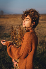 Portrait of a beautiful young woman with curly hair while enjoying the sun and hugging bouquet of reeds