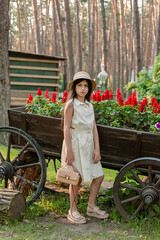 Dark-haired tween girl posing near vintage wooden cart used as flower bed in park