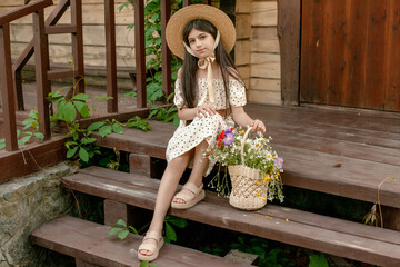 Dark-haired tween girl sitting on wooden doorstep with basket of wildflowers