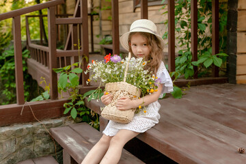  ute little girl sitting on country house threshold with basket of wildflowers