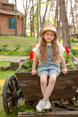 Dreamy preteen girl sitting on vintage wooden cart decorated as flower bed at country estate
