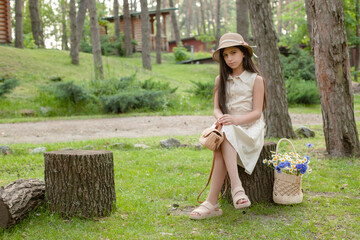 Preteen brunette resting on tree stump during walk in green park in summer