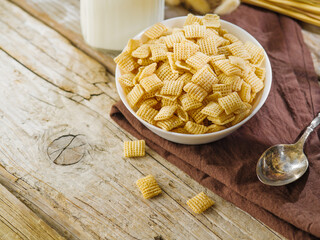 Quick whole grain breakfast - a bowl of crispy pads, a spoon, a jug of milk. Isolated on a wooden background. Express breakfasts, children's and diet food. Advertising, banner.