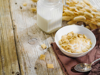 A bowl with cereal pads filled with milk, a jug of milk, a bunch of cereals on a wooden background. Solar lighting. Fast breakfast cereals, organic food, healthy nutrition, diet, fitness, baby food.
