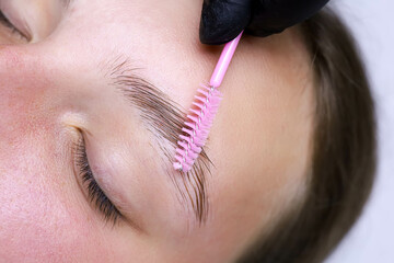 combing the eyebrow hairs after the eyebrow lamination procedure with a pink brush