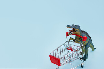 Toy dino pushes a shopping cart on a blue background. Sale season concept. Selective focus, copy...