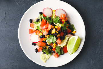 Plate of Mexican vegetable salad with black beans and radish on dark background, closeup