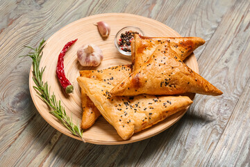 Plate with tasty Uzbek samsa and spices on wooden background