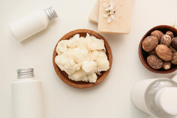Bowl of shea butter, nuts and cosmetics on light background