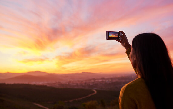 I want to remember this forever. Rearview shot of a woman taking a photo of a sunset with her smartphone.