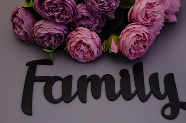 A bouquet of peonies and a wooden sign "Family" on a gray background. Recognition of feelings, tenderness and attention.