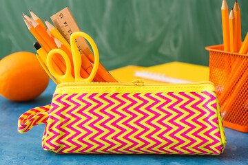 Pencil case with stationery on table against blackboard, closeup