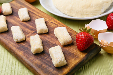Board with raw lazy dumplings and strawberry on color wooden background, closeup