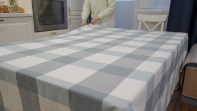 Woman spreading tablecloth and placing vase with bouquet of flowers on dining table in the kitchen. High quality 4k footage
