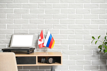 Workplace with laptop, flags of Canada and Russia near grey brick wall