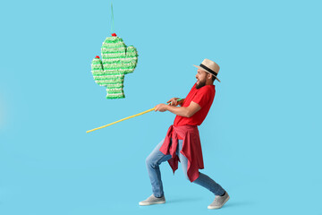 Handsome man breaking Mexican pinata on color background