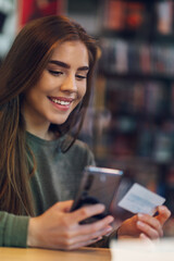 Woman using smartphone and a credit card for online shopping in a cafe