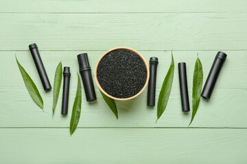 Composition with bowl of activated carbon powder, bamboo sticks and leaves on color wooden background