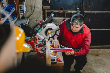 Fototapeta premium One man caucasian adult male working by the circular saw and work tools at garage workshop real people copy space hobby and craft concept