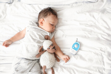 Adorable little child with toy and baby monitor sleeping on bed