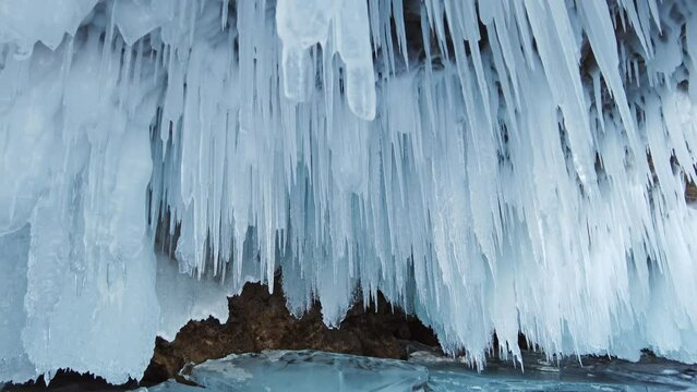 Ice cave on Baikal lake in winter. Clear transparent ice and icicles in grotto. Olkhon island, Baikal, Siberia, Russia, tilt view 4k