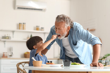 Little boy giving blackberry to his grandfather in kitchen