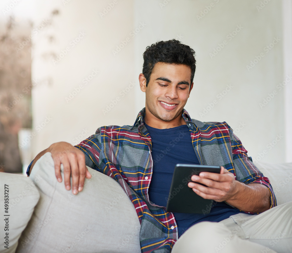 Poster staying connected to the world. shot of a handsome young man using his tablet while relaxing on the 