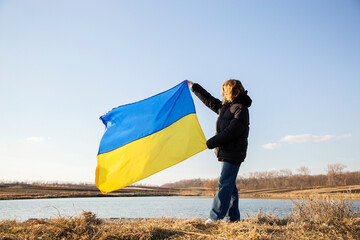 Ukrainian yellow-blue flag against the sky in the hands of a young woman. National symbol of...