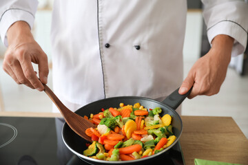 Male chef with spatula frying vegetables in kitchen, closeup