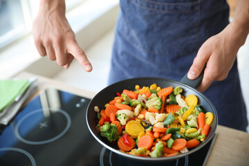 Young man pointing at frying pan with tasty vegetables in kitchen, closeup