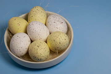 yellow easter eggs in white bowl on blue background, copy space	