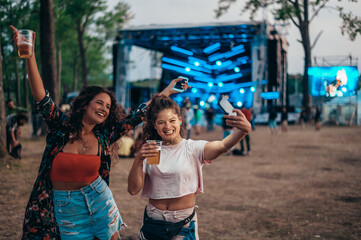 Obraz na płótnie Canvas Two beautiful friends taking a selfie with a smartphone on a music festival