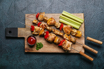Wooden board of grilled chicken skewers with vegetables and sauce on black background