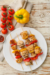 Plate of grilled chicken skewers with vegetables on white wooden background