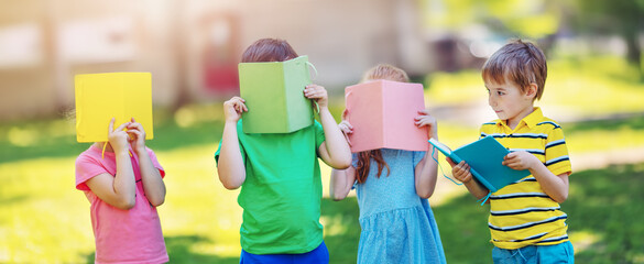 Children standing in the park covered faces with books.