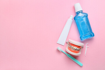 Model of jaw with dental braces, tooth brush, paste and rinse on pink background