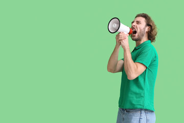 Angry young man shouting into megaphone on green background