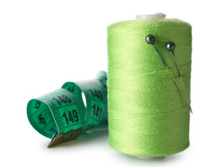 Green sewing thread spool with pins and measuring tape on white background