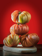 Close-up of four ripe tomatoes placed on a wooden board, forming a pyramidal figure. Red background. Beefsteak tomatoes.